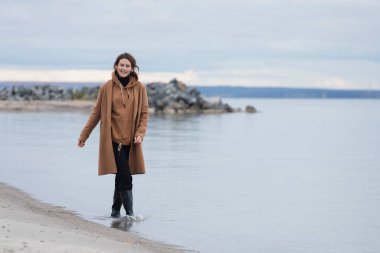 Bej renkli yün ceketli güzel bir mankenin portresi güneşli bir sonbahar gününde arka planda, günün tadını çıkar. Kadınların ve doğanın birliği kavramı, barışçıl ruh hali.