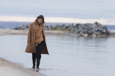 Bej renkli yün ceketli güzel bir mankenin portresi güneşli bir sonbahar gününde arka planda, günün tadını çıkar. Kadınların ve doğanın birliği kavramı, barışçıl ruh hali.