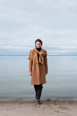 Sahilde yürüyen ve denize karşı sıcak kıyafetler giyen genç bir kadın. Köyde yaz tatili ve yaşam tarzı kavramı, Seascape