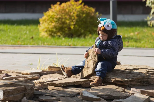 小さな1 2歳の幼児の男の子が遊び場で石で遊んで遊んでいるので 子供はフクロウの帽子で青いジャケットを着ています — ストック写真