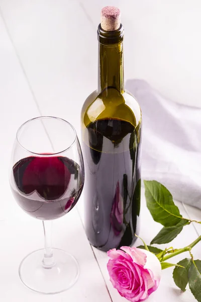 Το γυάλινο μπουκάλι κρασί με τα φελλούς και αυξήθηκε σε λευκά ξύλινα TA — Φωτογραφία Αρχείου