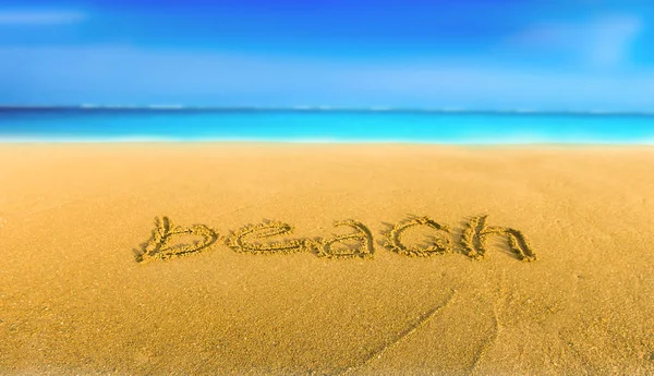 Желтый песок на пляже голубое море и надпись пляж — стоковое фото