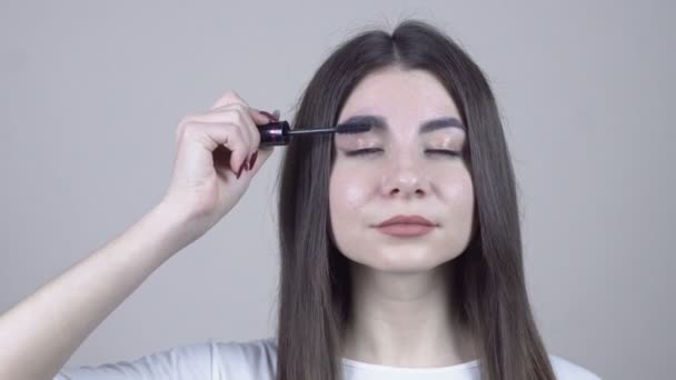 Bruneta kráska dívka použití make-up přes šedé pozadí. Řasenka. — Stock video