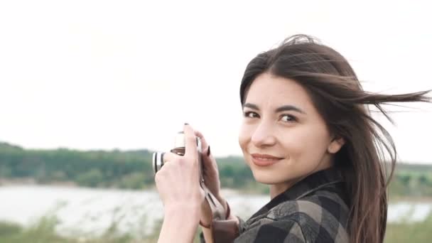 Krásná brunetka dívka dělá fotografa, na sobě tričko natáčení se starou analogovou kamerou — Stock video