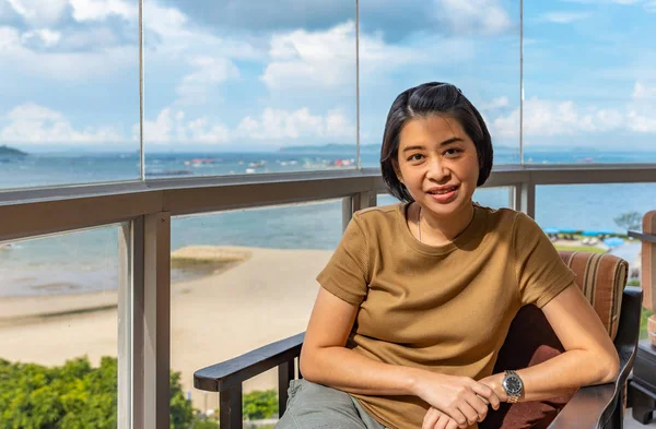 Turist Asyalı kadın kanepede oturuyor. Deniz manzarası arka plan. Orta yaşlı Asya veya Tay kadın portresi.