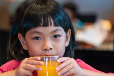 Asyalı küçük kız portakal suyu içiyor