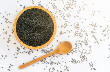 Tahta kâse ve kaşıkta siyah susam tohumları. Tahta beyaz masaya yayılan siyah susam tohumları. Hafif sıcak tonda. Düz konum şablon tasarımı, kopyalamak için boşluk.