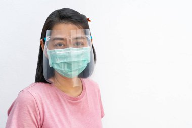 Asyalı orta yaşlı kadın portresi, tıbbi maske takıyor ve yüz maskesi takıyor, siyah kısa saçlı ve tişört giyiyor, kameraya bakıyor, beyaz arkaplanda izole bir görüntü var. Dosyada yol kırpılıyor.