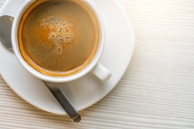 Sıcak kahve ya da beyaz masanın güzel dokusunda beyaz bardakta Americano, ekin görüntüsü, yazı için yer. Beyaz fincanda sıcak kahve, paslanmaz kahve kaşığı..