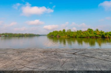 Ürün gösterisi için eski kırık ahşap masa, Asya 'daki bulanık nehir ve ağacın arka planı, mavi gökyüzü ve bulutlar, sıcak ışık tonu görüntüsü. Tasarım ve ürün sunumu için boş alan.
