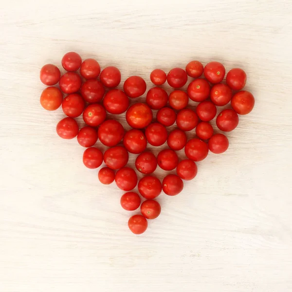 heart symbol of small red tomatoes on a light wooden background top view / favorite vegetables for healthy eating