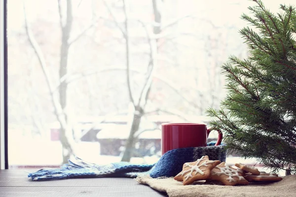 マグカップと冬のウィンドウの背景に緑の木の下で横になっている クリスマス前に雰囲気を温暖化図ジンジャー クッキーをスライドします — ストック写真