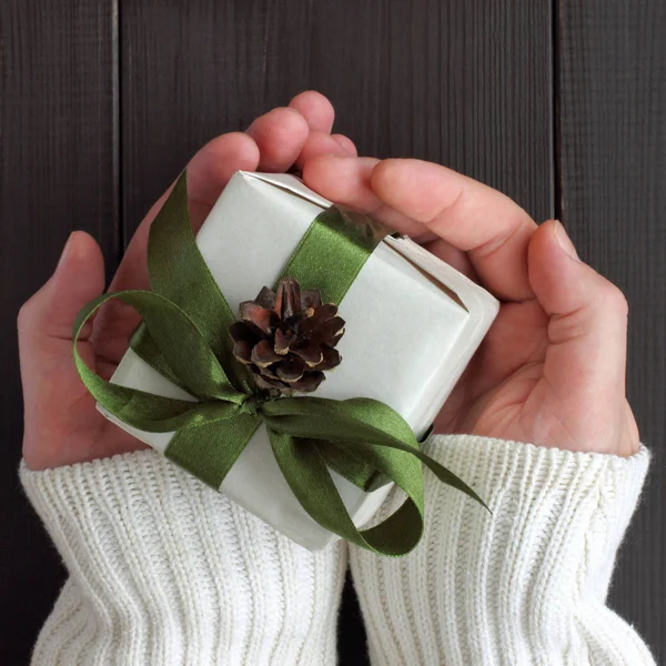 hands holding gift tied with a ribbon, decorated with fir cones / greetings on the winter holidays