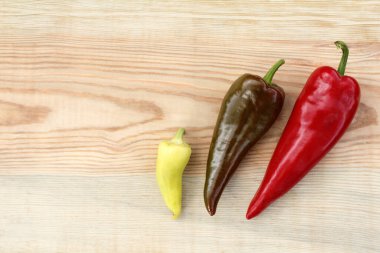 Tahta bir masanın üstünde her bir tat için üç farklı biber meyvesi.