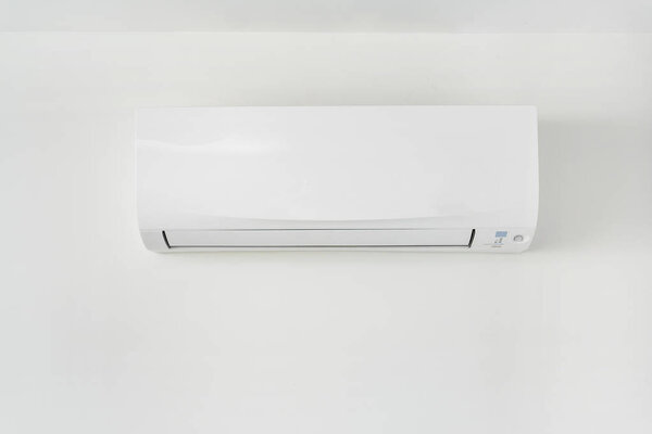 Air conditioner on white concrete wall in area of room space.