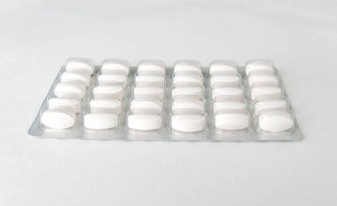 Beyaz arka planda beyaz haplar paketlenmiş. Eczane ve ilaç geçmişi için plastik pakette kapsül hapları.