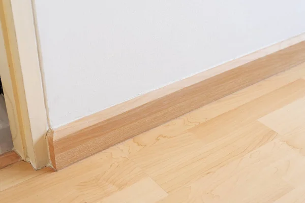 Wooden wall base skirting, finishing material with wood laminate floor and white mortar wall. Empty room with white wall and wooden floor new clean modern design.