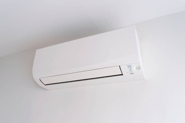 Air conditioner on white concrete wall in area of room space.