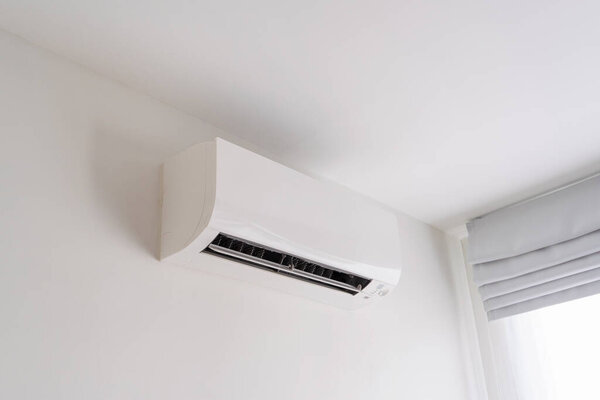Air conditioner on white concrete wall in area of room space.