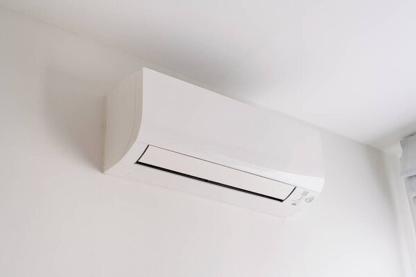Air conditioner on white concrete wall in area of room space.