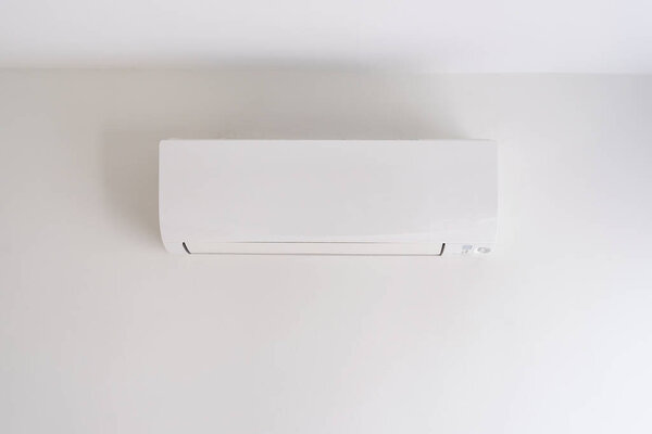 Air conditioner on white concrete wall in area of room space.