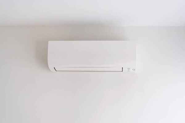 Air conditioner on white concrete wall in area of bedroom space.