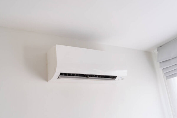 Air conditioner on white concrete wall in area of bedroom space.