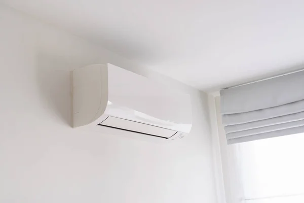 Air conditioner on white concrete wall in area of bedroom space.