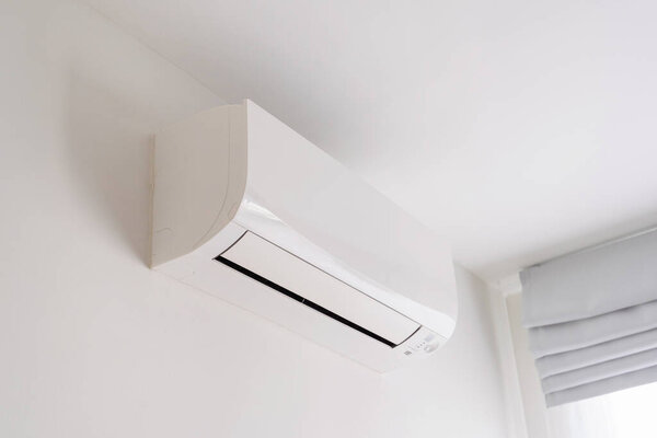 Air conditioner on white concrete wall in area of bedroom space.