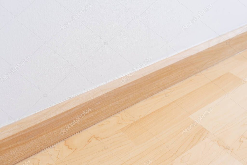 Wooden wall base skirting, finishing material with wood laminate floor and white mortar wall. Empty room with white wall and wooden floor.