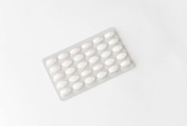 Beyaz arka planda beyaz haplar paketlenmiş. Eczane ve ilaç geçmişi için plastik pakette kapsül hapları.