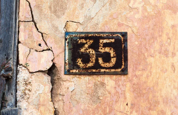 Number 35 on wall sign, rusty and weathered.