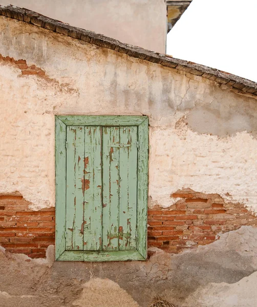 Old wooden window with green shutters on weathered wall.