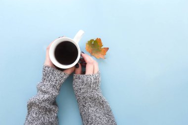 Bir sonbahar yaprak taze demlendi siyah kahve holding eller, düz mavi arka plan üzerinde yatıyordu..