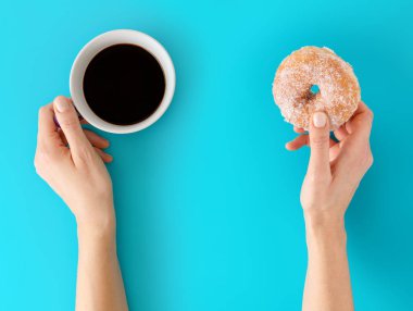 Bir fincan sade kahve ve çörek, holding eller arka plan mavi.