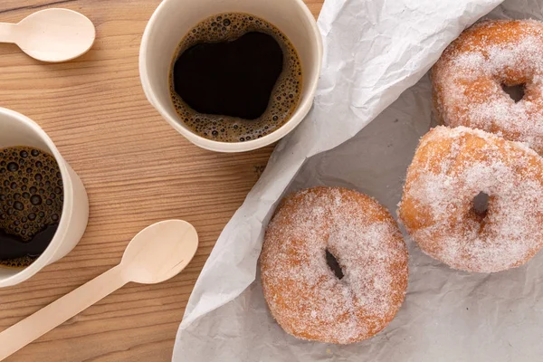 Sugar coated doughnuts on crumpled paper with two hot cups of coffee , on wooden background.