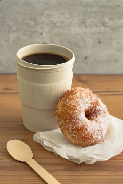A sugar coated doughnut on crumpled paper with a hot cup of coffee , on wooden background.