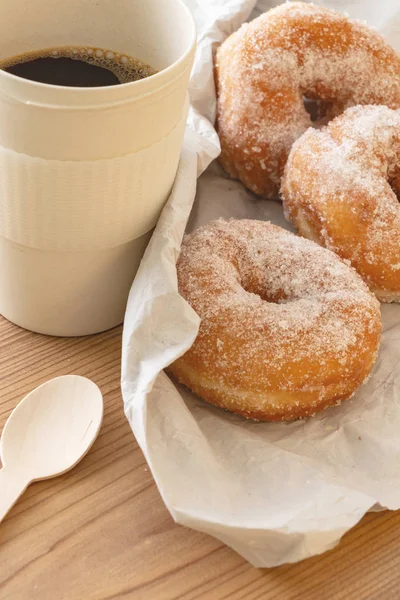 Sugar coated doughnuts on crumpled paper with a cup of coffee , on wooden background.