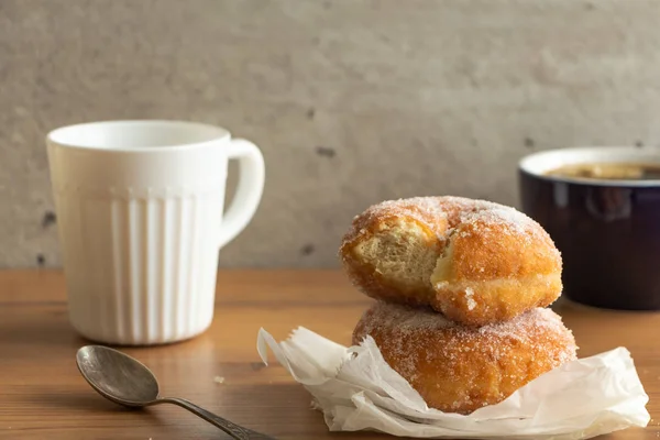Sugar coated doughnuts on crumpled paper with a two cups of coffee , on wooden tabletop.