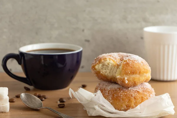 Sugar coated doughnuts on crumpled paper with a two cups of coffee , on wooden tabletop.