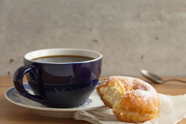 Sugar coated doughnut on crumpled paper with a cup of coffee , on wooden tabletop.