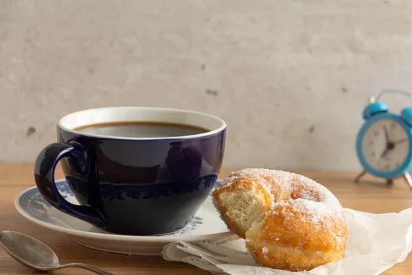 Sugar coated doughnut on crumpled paper with a cup of coffee , on wooden tabletop.