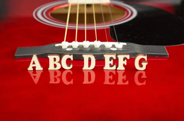 Notele muzicale ABCDEFG cu litere din lemn, pe suprafața reflectată a unei chitare acustice. Perspectiva podului chitarelor. Fundal creativ . — Fotografie, imagine de stoc