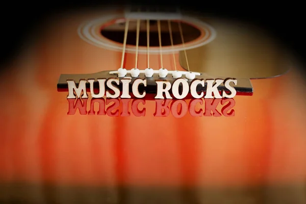 Cuvinte Muzică Rocks cu litere din lemn, pe suprafața reflectând o chitară acustică. Perspectiva podului chitarelor. Fundal creativ . — Fotografie, imagine de stoc