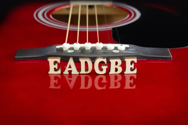 Note musicali EADGBE in corrispondenza di arrangiamento d'archi, con lettere di legno, su superficie riflettente di una chitarra acustica. Chitarre bridge prospettiva. Sfondo creativo . — Foto Stock