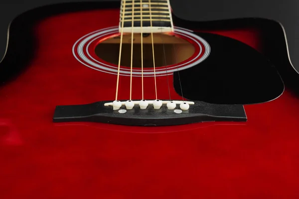 Closeup of a six stringed red acoustic guitar, from bridge side. Music entertainment background. — Stock Photo, Image