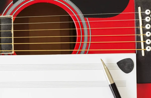 Blank music notebook page with copy-space, on red guitar with six strings. With pen and black guitar pick. Musical education concept.