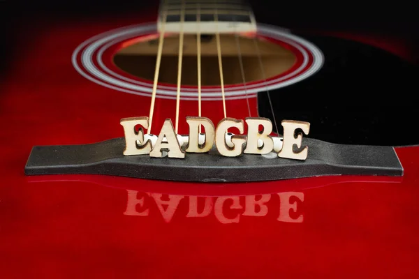 Müzik notları Eadgbe bir akustik gitar Köprüsü üzerinde, ahşap harfler ile dizeleri düzenlemesi karşılık gelen. Gitar Köprüsü perspektifi. Yaratıcı arka plan. Stok Fotoğraf