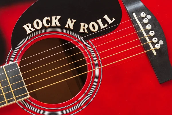 Words Rock N Roll con lettere in legno, primo piano su una superficie di chitarra acustica rossa. Musica sfondo intrattenimento . — Foto Stock