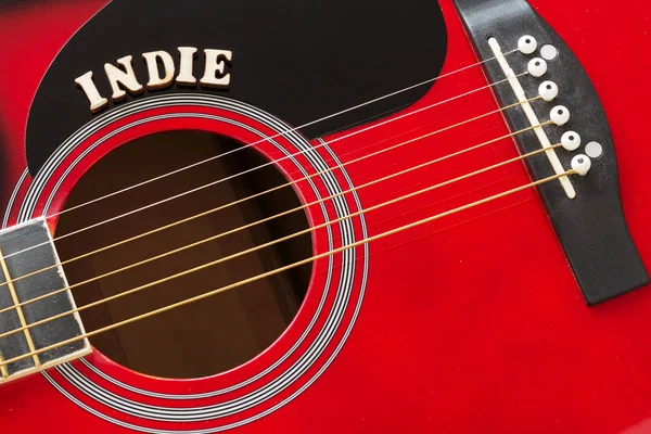 Word Indie con letras de madera, primer plano en una superficie de guitarra acústica roja. Fondo de entretenimiento musical . — Foto de Stock